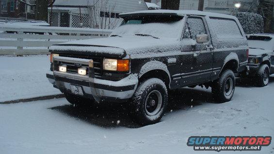 Dark Ford Bronco covered in snow, parked next to another vehicle