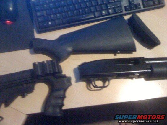 Disassembled black shotgun with pistol grip and stock on a wooden surface next to a keyboard