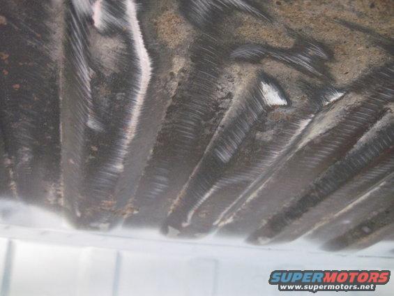 Underside of a vehicle showing ribbed metal and some rust. Supermotors.net logo visible