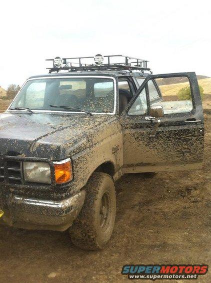 Mud-covered Ford F-Series truck with roof rack and open driver's door