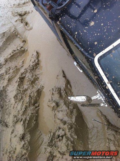 Black SUV with mud splatters stuck in deep mud, showing tire tracks and a side mirror