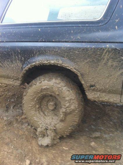Mud-covered tire and fender of a dark-colored vehicle stuck in mud
