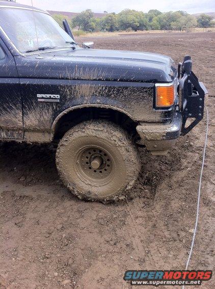 Black Ford Bronco covered in mud, front wheel stuck in mud, aftermarket bumper with spare tire mount