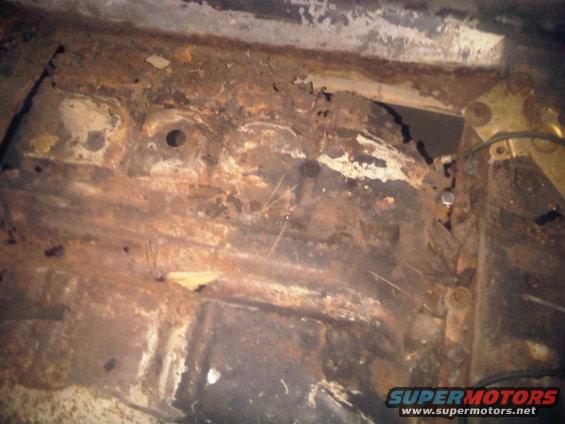 Heavily rusted metal structure, possibly part of a car's undercarriage, with visible holes and damage