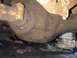 1973 Ford Ranchero - The underside of a vehicle's rear axle is visible, with some exhaust pipes overhead and a cluttered background.