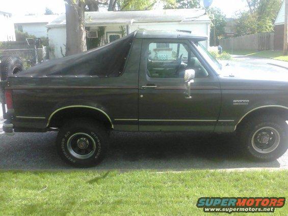 Side view of a dark green 1988 Ford Bronco with a black soft top covering the rear