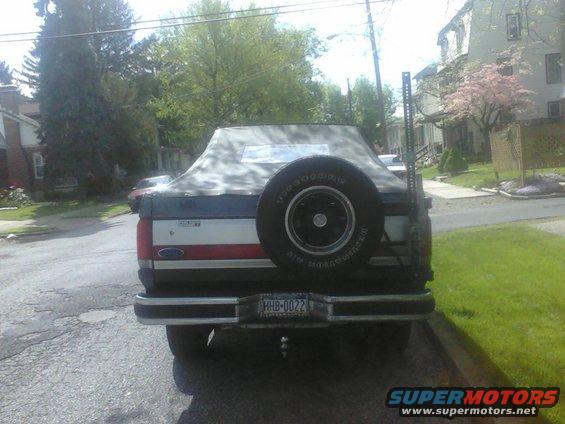 Rear view of a 1987 Ford Bronco with a soft top and spare tire mounted on the back. The license plate reads HHB-0022