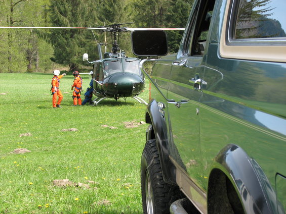Side view of a green SUV parked next to a helicopter with people in orange suits