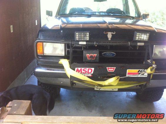 Front of a black Ford truck with a bull skull emblem on the hood, a winch, and yellow tow straps