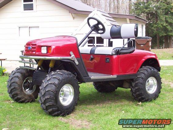 Red golf cart with large off-road tires and a Ford emblem on the grille