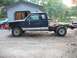 1994 Ford Explorer - A dark blue pickup truck chassis with a cab sits in a dirt lot next to a garage, with another vehicle partially visible in the background.