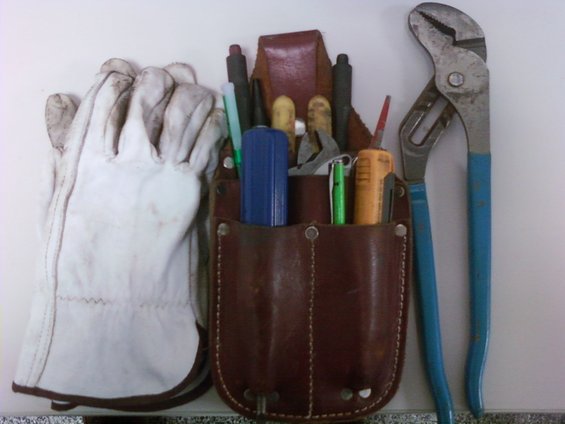 work gloves next to a leather tool belt with pliers and pens