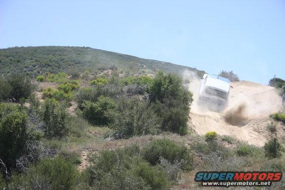 White SUV kicking up dust while driving down a dirt hill off-road