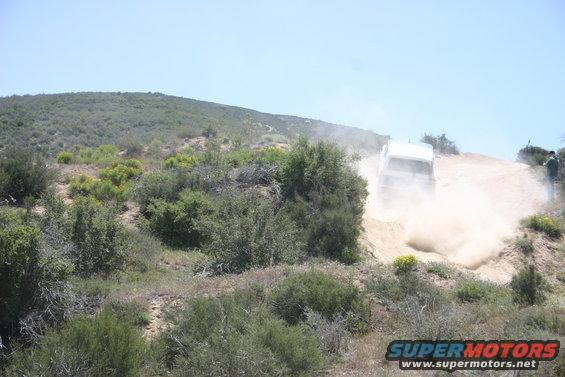 White SUV driving up a dusty hill, kicking up a lot of dirt