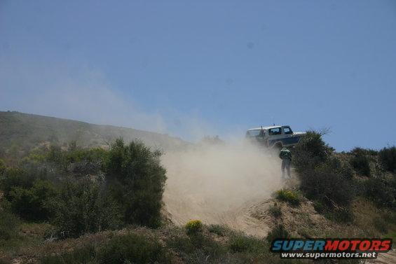 1991 Ford Bronco driving on a dusty hill, kicking up a large cloud of dirt