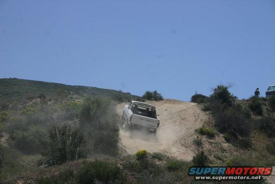 White 1991 Ford Bronco driving up a dirt hill, kicking up dust