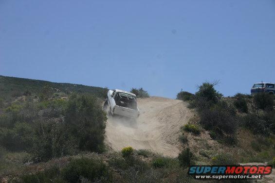 1991 Ford Bronco climbing a steep dirt hill, another vehicle visible on the ridge above