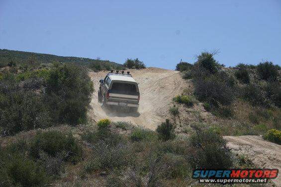 White 1991 Ford Bronco driving up a dirt hill, rear view