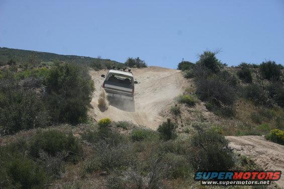 1991 Ford Bronco driving up a dusty dirt hill, kicking up dust