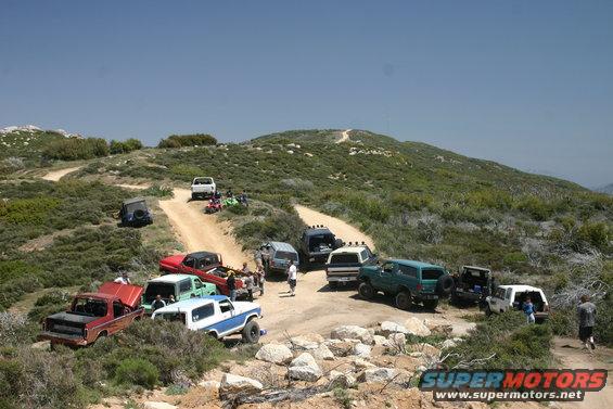 Group of off-road vehicles parked on a dirt trail in a hilly, scrub-covered area
