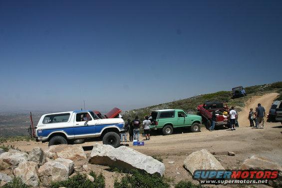 Blue and white 1978 Ford Bronco parked on a rocky hill with other vehicles