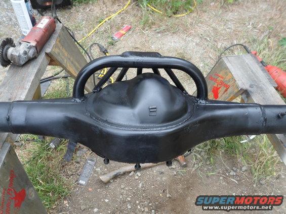 Black Ford rear axle assembly with a roll cage hoop welded on top, resting on sawhorses with grinders nearby