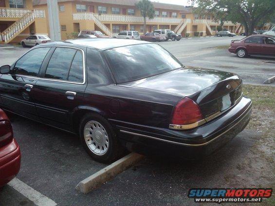 Black 2001 Ford Crown Victoria parked, rear quarter view. Red car partially visible on left