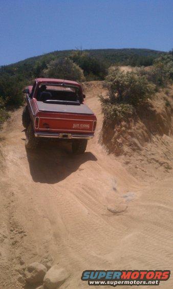 Red pickup truck with "BRONCO" text on tailgate driving off-road