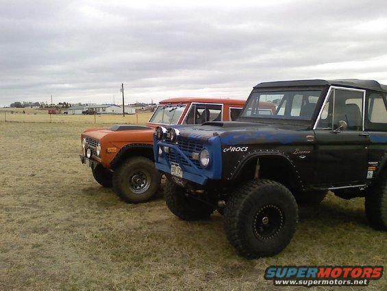 Black 1971 Ford Bronco with blue accents and orange Bronco behind it