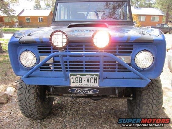 Front view of a blue 1971 Ford Bronco with two large off-road lights mounted on a custom bumper and grille