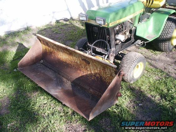 Green John Deere 400 tractor with a rusty front loader attachment parked on grass