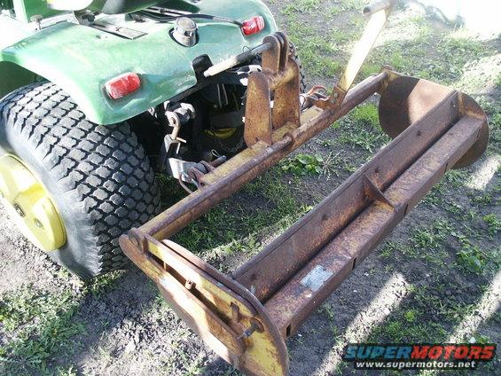 Green tractor rear with yellow attachment. Rusty metal