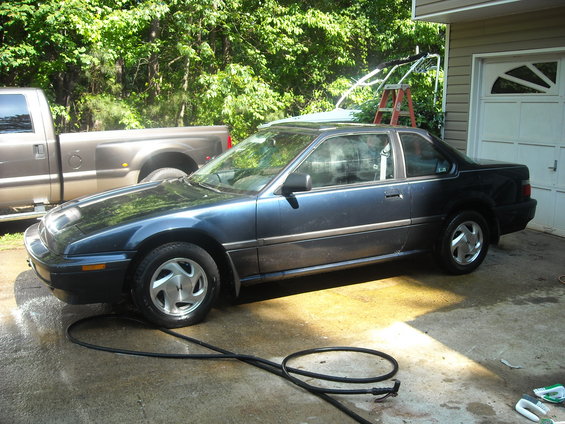 Blue coupe with pop-up headlights being washed next to a pickup truck