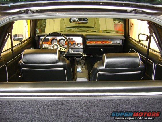 Car interior with black seats, dashboard with gauges, and a steering wheel. Flames are visible on the dashboard trim