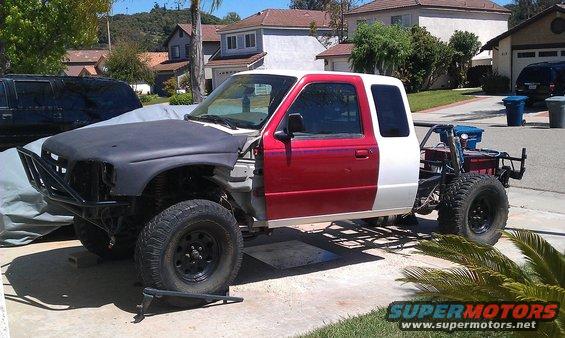 Red and white Ford Ranger truck with a custom roll cage and off-road tires, undergoing modifications