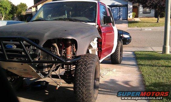 Modified Ford Ranger with off-road tires, custom bumper, and unfinished body panels