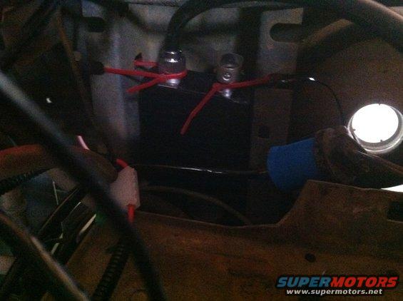 Close-up of a black battery with red wires connected to its terminals. Some blue insulation is visible