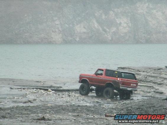 1978 Ford Bronco with lifted suspension driving on a rocky shore next to a body of water