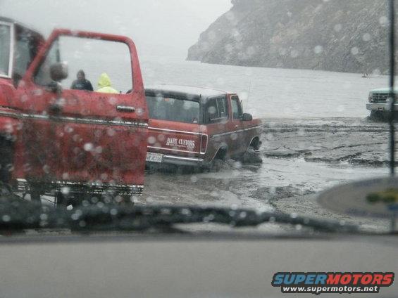 red pickup truck door open, red SUV stuck in mud with 'BAILEY CUSTOMS' on the side, another truck in background