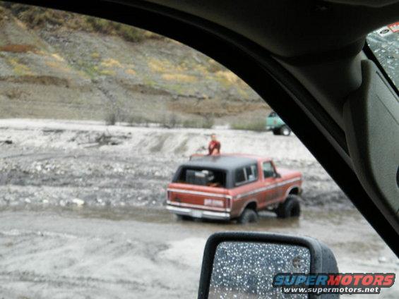 Red 1978 Ford Bronco driving through muddy water, rear view