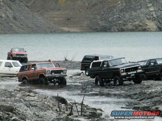 1978 Ford Bronco and other SUVs driving through shallow water and mud