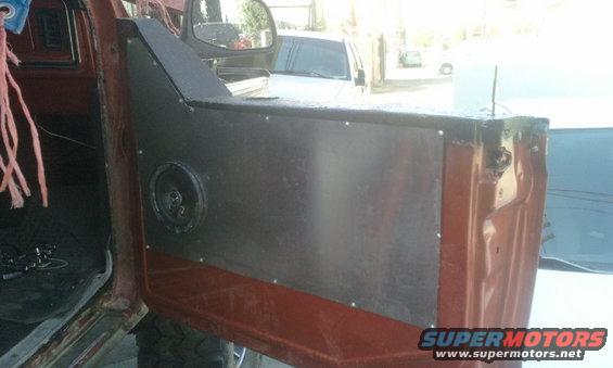 Brown interior door panel with a speaker and custom metal cover. A side mirror is visible