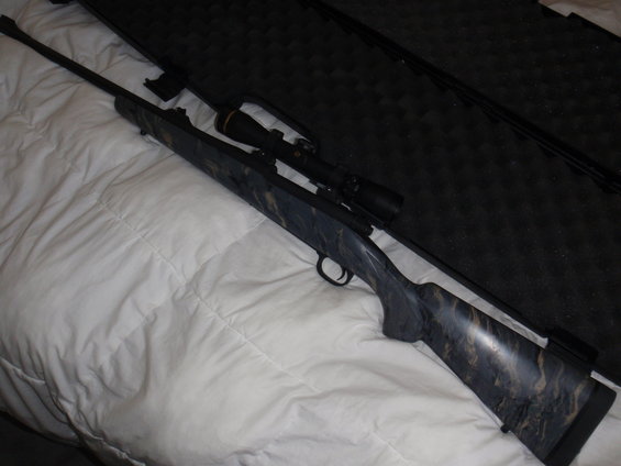 rifle with scope in a case, resting on a white comforter
