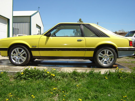 Yellow coupe parked outside a garage. Side view shows louvers on the rear window