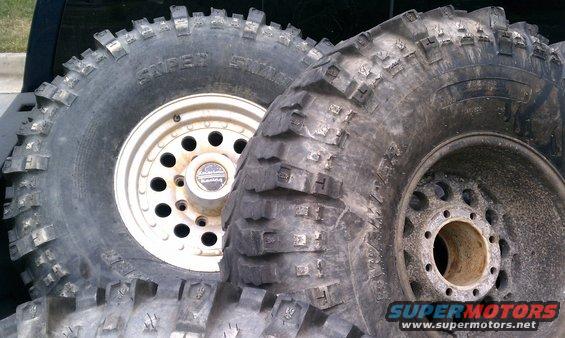 Two large off-road tires with aggressive tread patterns and one white rim with a center cap. Another tire is partially visible at the bottom
