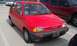1991 Ford Festiva - A red 1991 Ford Festiva is parked in a lot next to a red pickup truck.