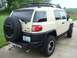 2010 Toyota FJ Cruiser - This tan Toyota FJ Cruiser is seen from the rear, a spare tire on the back and a roof rack. The FJ Cruiser badge is visible on the tailgate.
