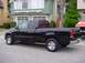 2001 Ford F-150 - A black 2001 Ford F-150 pickup truck is parked on a residential street next to a house and another vehicle.