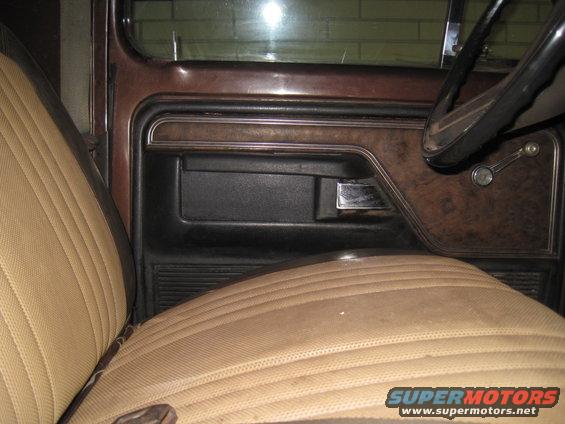 Passenger side door panel with wood grain trim, black armrest, and chrome handle. Tan seat with stitching visible