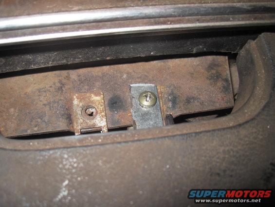 Rusted metal bracket secured with a screw, part of interior trim